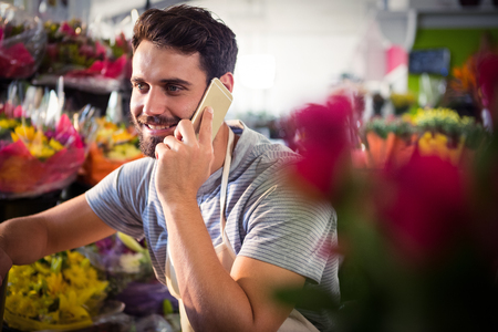 Male florist talking on mobile phone at his flower shopの写真素材