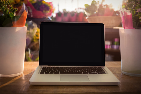 Close-up of flower vase and laptop on the wooden table at a flower shopの写真素材