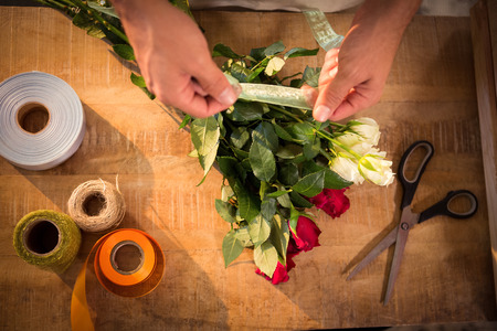 Close-up of male florist tying poly ribbon on bunch of flowers at his flower shopの写真素材