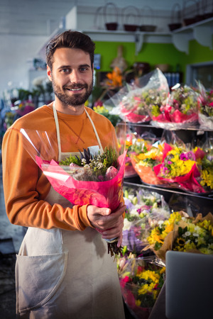 Portrait of male florist holding flower bouquet at his flower shopの写真素材