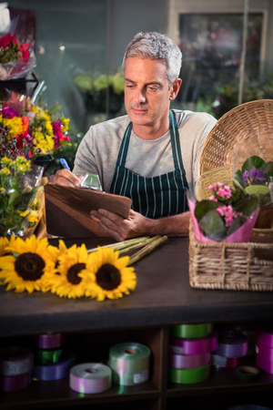 Male florist writing on clipboard at his flower shopの写真素材