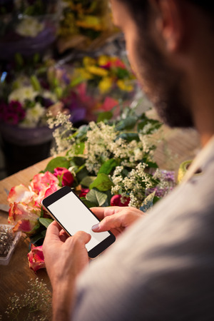 Male florist text messaging on mobile phone at his flower shopの写真素材