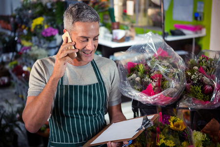 Male florist taking order on mobile phone at his flower shopの写真素材