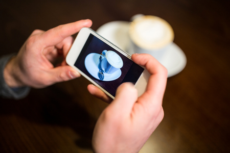 Man taking photo of coffee cup in restaurantの写真素材