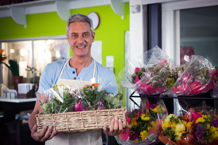 Portrait of male florist carrying plant pot in wicker basket at his flower shopの写真素材
