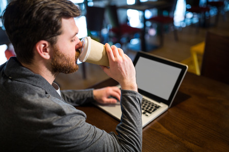 Man having coffee while using laptop in restaurantの写真素材