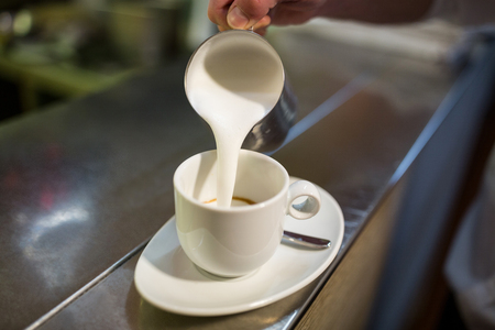Close-Up of waiter adding milk to coffee in restaurantの写真素材