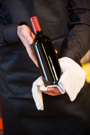 Mid section of waiter holding a bottle of red wine in restaurantの写真素材