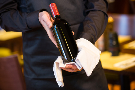 Mid section of waiter holding a bottle of red wine in restaurantの写真素材