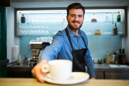 Portrait of waiter offering cup of coffee in restaurantの写真素材