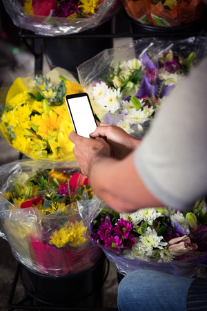 Mid section of male florist taking photo of flower bouquet on mobile phone at his flower shopの写真素材