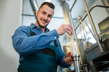Happy brewer checking beer with hydrometer at breweryの写真素材