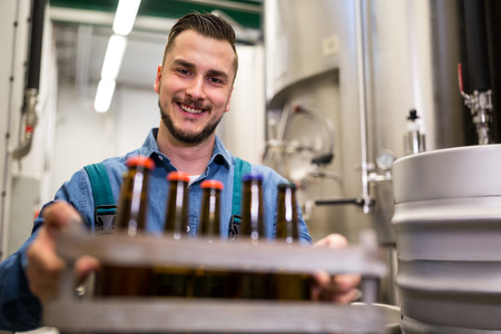 Portrait of happy brewer holding beer bottles in crate at breweryの写真素材