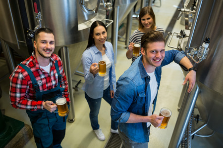 Portrait of happy brewers holding glass of beer standing at brewery
