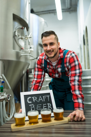 Portrait of happy brewer with four glasses of craft beer on table at breweryの写真素材
