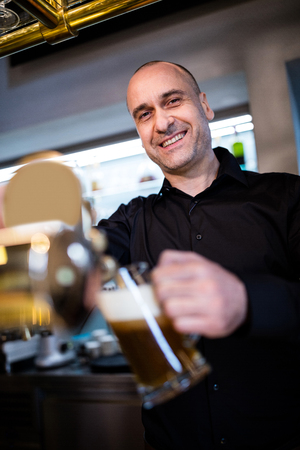 Portrait of smiling brewer filling beer in beer glass from beer pump in bar