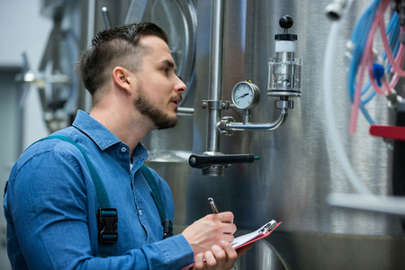 Attentive maintenance worker writing on clipboard at breweryの写真素材