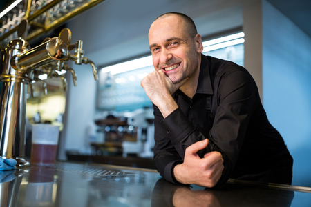 Portrait of happy bar tender leaning at bar counterの写真素材