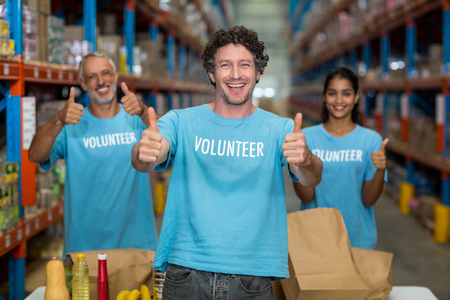 Portrait of happy volunteers are posing with thumbs up in a warehouse
