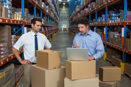 Managers working with a laptop put on a cardboard box in a warehouseの写真素材