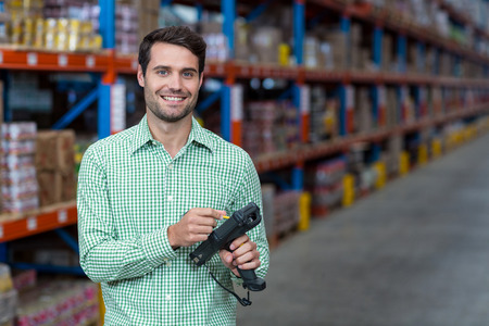 Happy worker holding a tool and smiling in a warehouseの写真素材