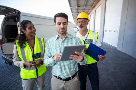 Worker is standing and looking a tablet in front of a warehouseの写真素材