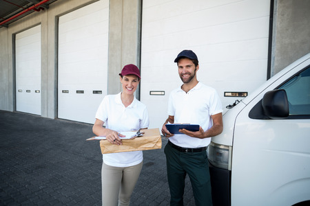 Portrait of delivery people are holding goods and posing in front of a warehouseの写真素材