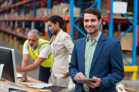 Focus on manager is smiling and holding a tablet in front of his colleagues in a warehouseの写真素材