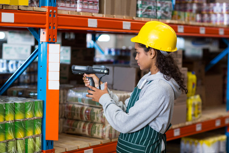 Female worker wearing yellow helmet scanning documents in warehouseの写真素材