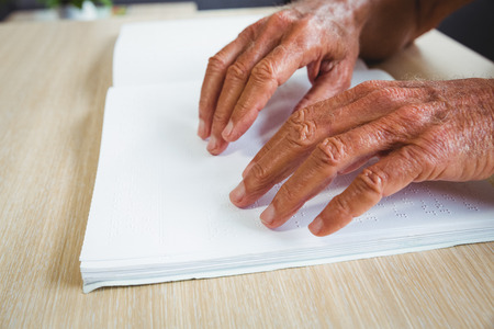 Senior man using braille to read in a retirement homeの写真素材