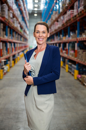 Business woman smiling with her clipboard in a warehouseの写真素材