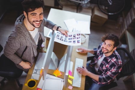 High angle portrait of happy photo editors working at computer desk in creative officeの写真素材