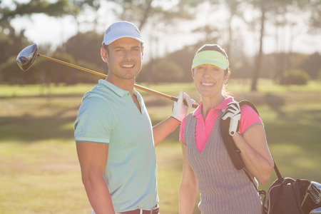 Portrait of smiling couple with bag and golf club while standing on fieldの写真素材