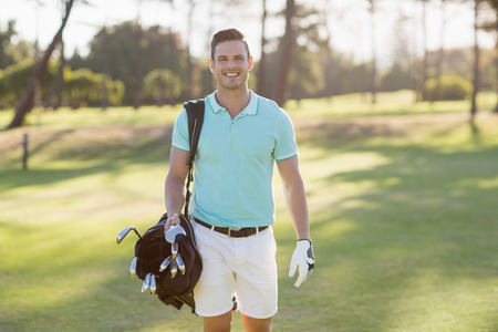 Portrait of smiling young man carrying golf bag while standing on fieldの写真素材