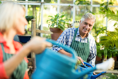 Happy man watering plants with woman at greenhouseの写真素材