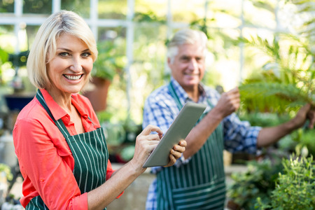 Portrait of happy woman using digital tablet while man working at greenhouseの写真素材