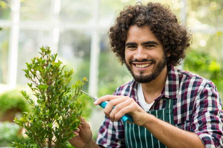 Portrait of happy male gardener pruning plants at greenhouseの写真素材
