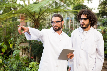 Male scientist pointing while standing by coworker outside greenhouse