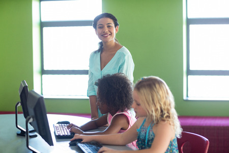 Portrait of confident teacher with children in computer class