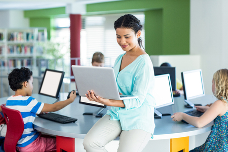 Smiling teacher using laptop during computer classの写真素材