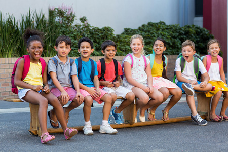 Portrait of smiling schoolchildren on seat outside schoolの写真素材