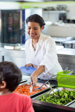 Smiling woman serving food to schoolboy in canteenの写真素材
