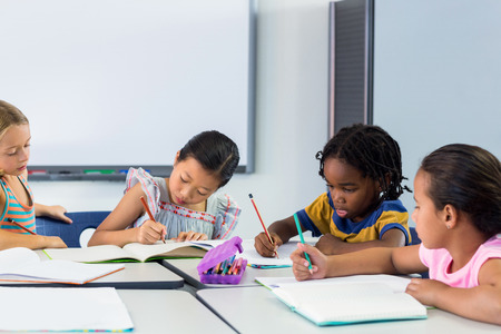 Schoolchildren writing on books in classroomの写真素材