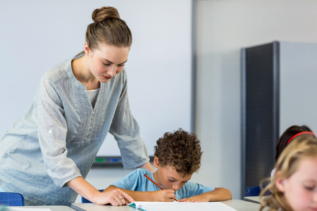 Female teacher looking at student writing on book in classroomの写真素材