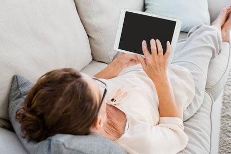 Woman using digital tablet while resting on sofa at homeの写真素材