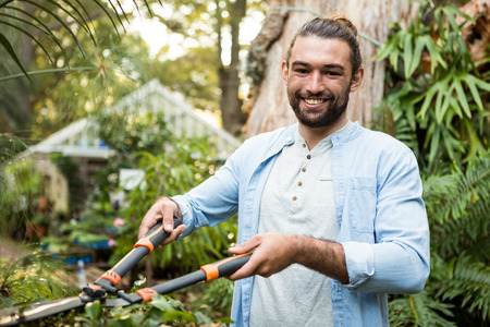 Portrait of happy young male gardener using hedge clippers at community gardenの写真素材