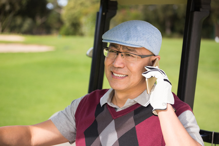 Golfer smiling and calling in his golf buggyの写真素材
