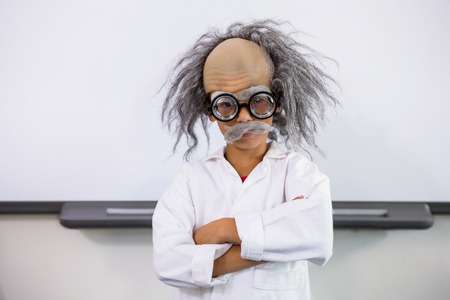Portrait of boy dressed as scientist standing with arms crossed in classroomの写真素材