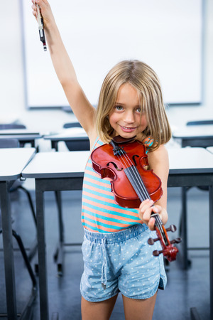 Portrait of happy girl playing violin in classroomの写真素材