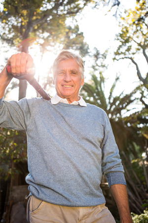 Portrait of happy mature male gardener carrying shovel on shoulder at gardenの写真素材